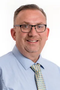 professional headshot of Dr. Roth wearing a yellow tie with a repeating pattern of blue squares