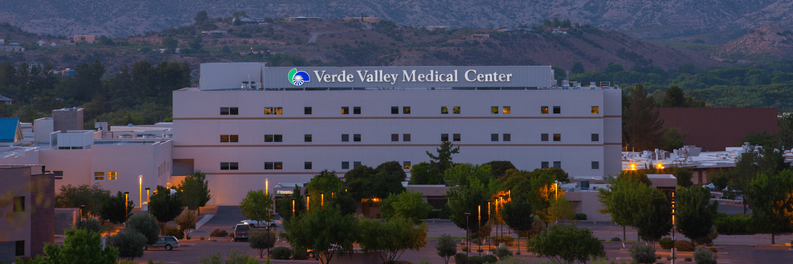 A view of Verde Valley Medical Center with surrounding trees and hills in the background, taken at dusk.